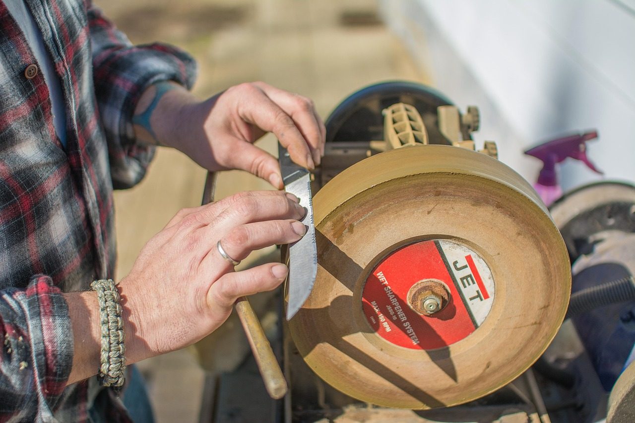 Hands sharpening a knife on a wet sharpening wheel outdoors