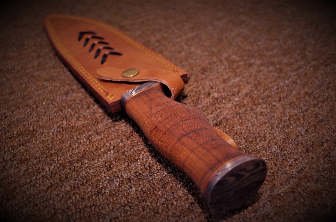 A knife with a wooden handle and a patterned metal pommel, in a leather sheath